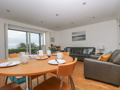 A dining table set with plates cups and scones in a living room with leather sofas and a sliding glass door at Rock Pool in Downderry