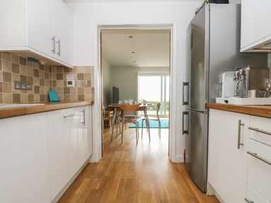 A kitchen with white cabinets and wooden countertops leading to a dining area with a wooden table and chairs at Rock Pool in Downderry