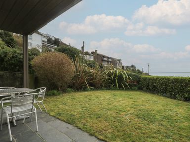 A garden with grass lawn metal table and chairs and houses in the background at Rock Pool in Downderry