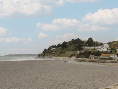 A sandy beach with a rocky hill and several houses under a cloudy sky at Rock Pool in Downderry