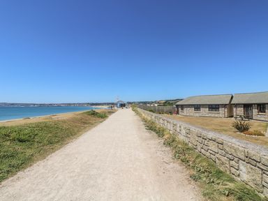 A sandy pathway along the coastline with buildings on the right and a cafe in the distance at Shoreline in Marazion