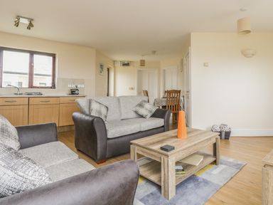 A living room with two sofas a wooden coffee table with an orange vase and a dining area at Shoreline in Marazion