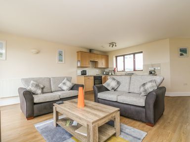 A living room with two sofas a wooden coffee table and an open kitchen at Shoreline in Marazion
