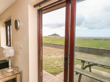 A view of an open glass door showing a picnic table outside and a clock lamp and table inside at Shoreline in Marazion