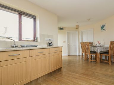 A kitchen area with wooden cabinets a sink and a dining table with chairs at Shoreline in Marazion