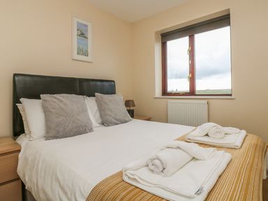 A bedroom with a bed with white linens and towels on a mustard throw by a window at Shoreline in Marazion