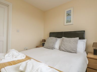 A bedroom with a made bed with white linens two grey pillows and towels on the end at Shoreline in Marazion