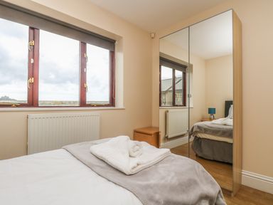 A bedroom with a bed folded towels a wooden nightstand a mirrored wardrobe and a window with a radiator below at Shoreline in Marazion
