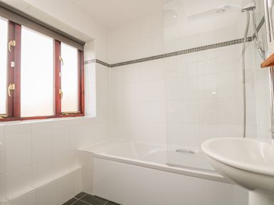 A bathroom with a bathtub shower combination a sink and a window at Shoreline in Marazion