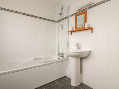 A bathroom with a bathtub shower combination and a pedestal sink with a mirror and shelf at Shoreline in Marazion