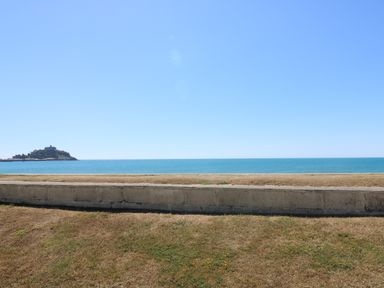 A view of the sea with a small island and a concrete wall in the foreground at Shoreline in Marazion
