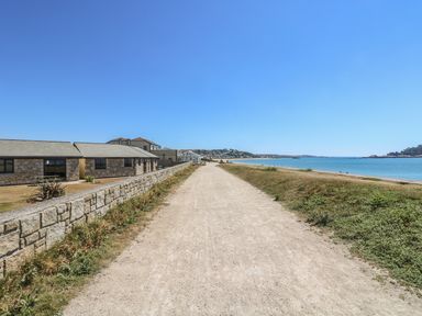 A sandy path between a stone wall and grassy area leading to the sea at Shoreline in Marazion
