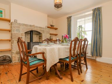 A dining room with a table set for four near a stone fireplace and a window with blue striped curtains at 1 Dormer Villas Portscatho