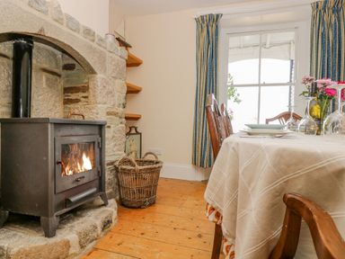 A dining room with a wood burning stove stone hearth wicker basket and a table set with plates wine bottle and glasses at 1 Dormer Villas in Portscatho