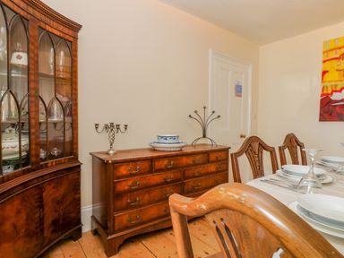 A dining room with wooden chairs a wooden sideboard and a glass cabinet at 1 Dormer Villas in Portscatho