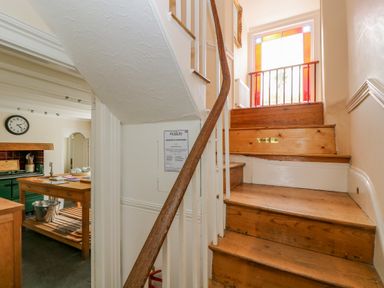 A wooden staircase with a handrail and stained glass window next to a kitchen with a clock and wooden furniture at 1 Dormer Villas in Portscatho