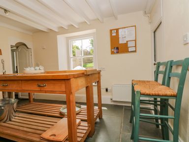 A kitchen with a wooden island table and green chairs against the wall at 1 Dormer Villas Portscatho