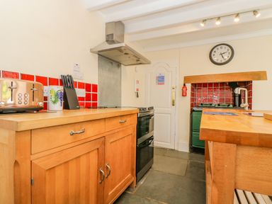 A kitchen with wooden cabinets red tiled backsplash a clock on the wall and a green stove at 1 Dormer Villas in Portscatho