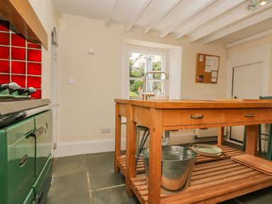 A kitchen with a wooden island and metal bucket next to a green stove with red tiles at 1 Dormer Villas in Portscatho