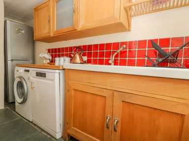 A kitchen with wooden cabinets red tiled backsplash a washing machine dishwasher refrigerator and a sink with dish rack at 1 Dormer Villas Portscatho