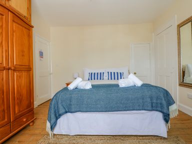A bedroom with a bed with blue blanket and striped pillows wooden wardrobe a mirror and two doors at 1 Dormer Villas in Portscatho