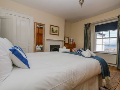 A bedroom with a bed pillows and rolled towels near a window with curtains and a chest of drawers at 1 Dormer Villas Portscatho