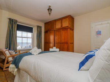 A bedroom with a bed and wooden wardrobe near a window at 1 Dormer Villas in Portscatho