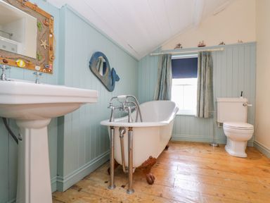 A bathroom with a freestanding clawfoot bathtub sink toilet and a window with curtains at 1 Dormer Villas Portscatho