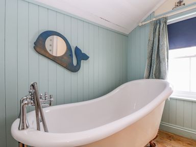 A bathroom with a freestanding bathtub a whale-shaped mirror and a window with curtains at 1 Dormer Villas in Portscatho