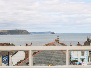 A coastal view from a window showing rooftops of buildings and the sea with cliffs in the background at 1 Dormer Villas in Portscatho