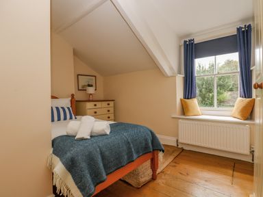 A bedroom with a bed with blue and white bedding a dresser a framed picture a window with blue curtains and yellow cushions at 1 Dormer Villas in Portscatho