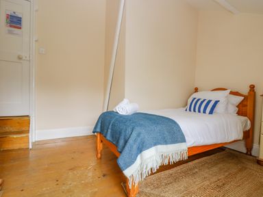A bedroom with a single bed made with white sheets a blue blanket and a striped pillow at 1 Dormer Villas in Portscatho