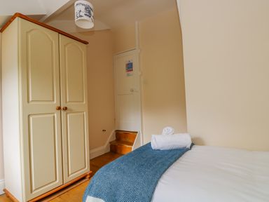 A bedroom with a bed with blue throw and towels and a cream wardrobe at 1 Dormer Villas in Portscatho