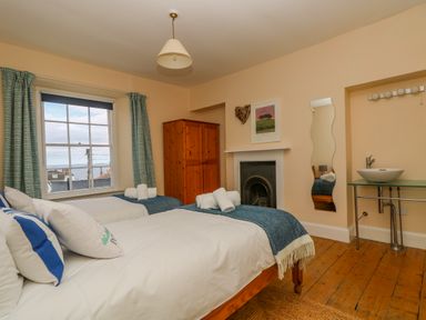 A bedroom with two beds a wardrobe a fireplace a wall mirror and a washbasin at 1 Dormer Villas in Portscatho
