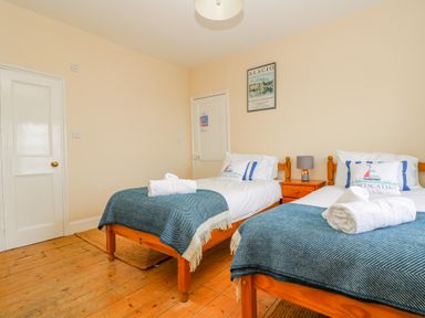 A bedroom with two single beds side by side with blue blankets and white rolled towels on wooden floors at 1 Dormer Villas Portscatho