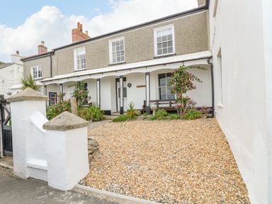 The front exterior of a two-story house with a gravel driveway and a porch with flowers at 1 Dormer Villas in Portscatho