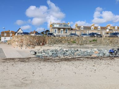 A sandy beach with rocks and a bicycle next to a stone seawall with buildings and cars behind at Mount View in Marazion