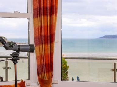 A telescope by a window with orange and red striped curtains overlooking a beach and ocean at Mount View in Marazion