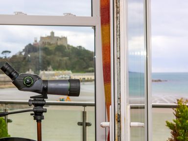 A telescope on a tripod by an open window overlooking a castle and the sea at Mount View in Marazion