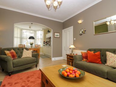 A living room with green sofas pillows fruit bowl on wooden table and dining area at Mount View in Marazion