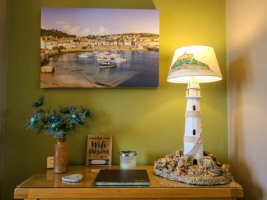 A table with a lighthouse lamp flowers a candle and a wifi password sign under a photo of a harbor at Mount View in Marazion