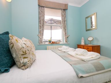 A bedroom with a bed with pillows and towels next to a window with curtains and a wooden dresser with a mirror and decoration at Mount View in Marazion