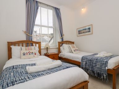 A bedroom with two single beds a nightstand with a lamp and a window with curtains at Mount View in Marazion