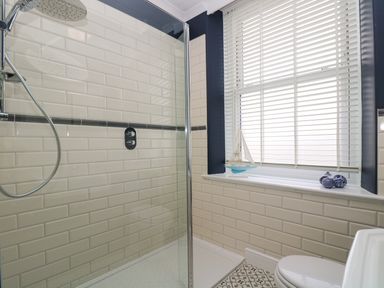 A bathroom with a shower with glass screen tiled walls a window with blinds and decorative items on the ledge at Mount View in Marazion