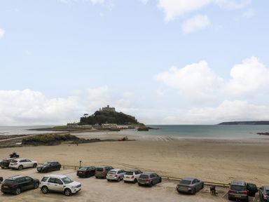 A beach parking area with multiple cars parked and a castle on a hill in the background near the sea at Mount View in Marazion