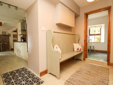 A hallway with a wooden bench and cushions leading to a kitchen and another room at Chenalls Cottage in Helston