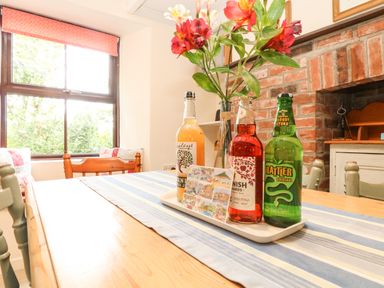 A dining table with bottles and flowers on a tray next to a window and brick fireplace at Chenalls Cottage in Helston