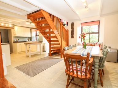 A kitchen and dining area with wooden stairs and a table with flowers at Chenalls Cottage in Helston