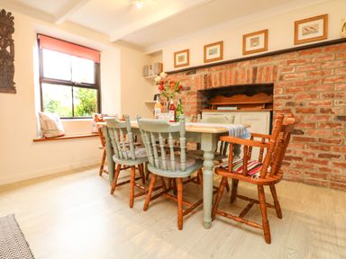 A dining room with a wooden table and chairs next to a brick fireplace at Chenalls Cottage in Helston