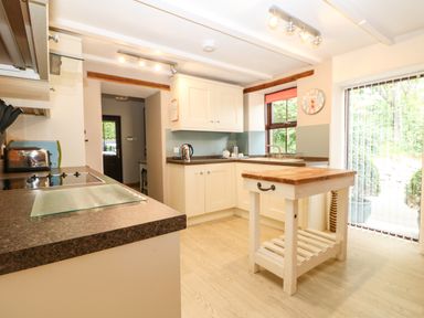 A kitchen with white cabinets a small wooden island a toaster and kettle at Chenalls Cottage in Helston